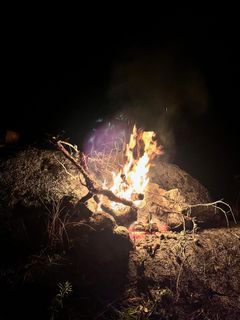 A small fire catching on dry branches against a granite boulder in the dark