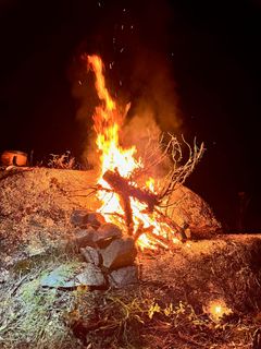 Tall flames and sparks rising from a stacked stone firepit at night