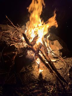 A crisscross of long sticks blazing against a rock wall at night